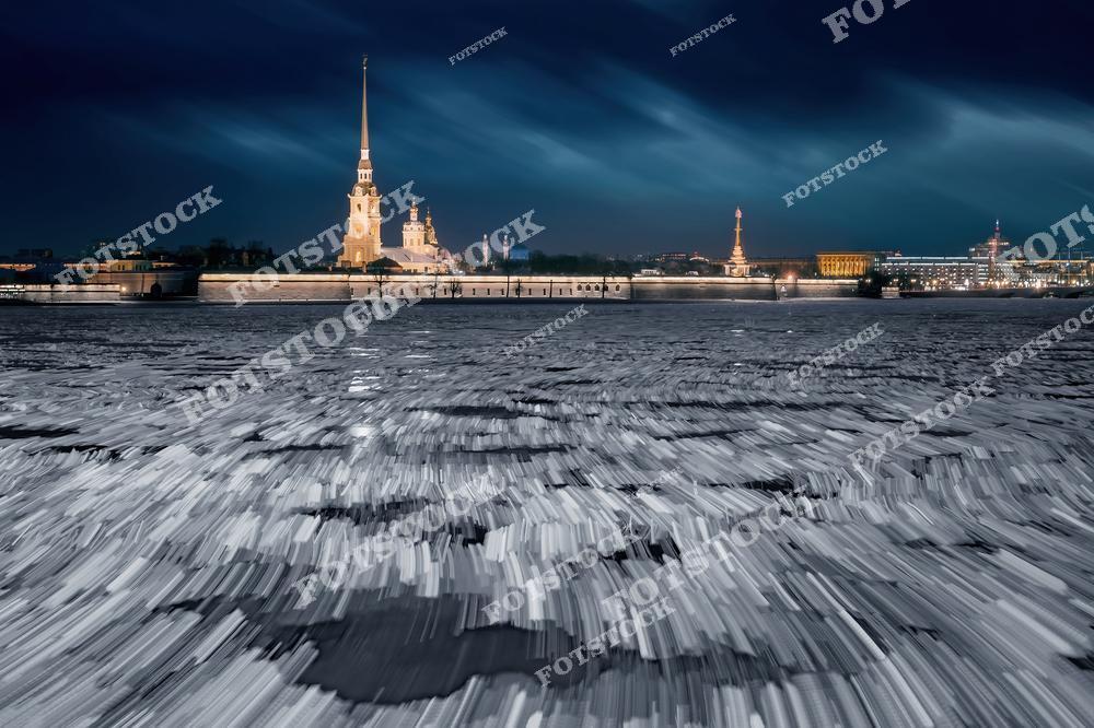 На фотографии изображена Петропавловская крепость на фоне зимней ночи. Замерзшая Нева покрыта льдинами, создавая эффектную текстуру на переднем плане. Подсветка крепости и окрестных зданий подчеркивает их историческое значение и красоту. Эта композиция — одно из самых знаковых изображений Санкт-Петербурга в зимний период.